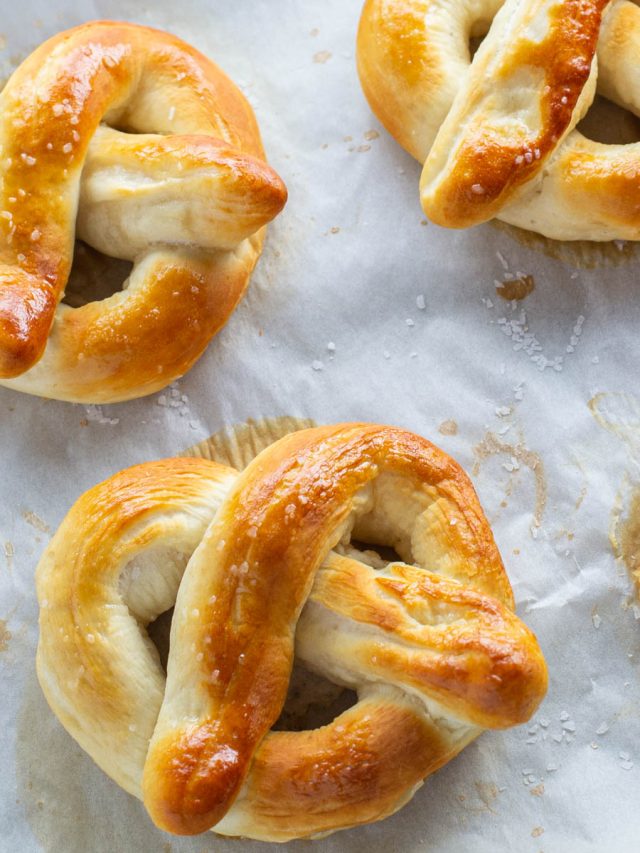 Golden-brown pretzels sprinkled with coarse salt, resting on parchment paper.