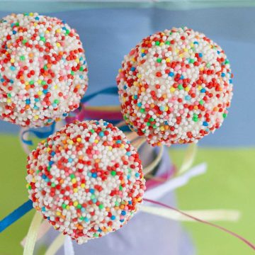 Three cake pops decorated with colorful candy sprinkles.