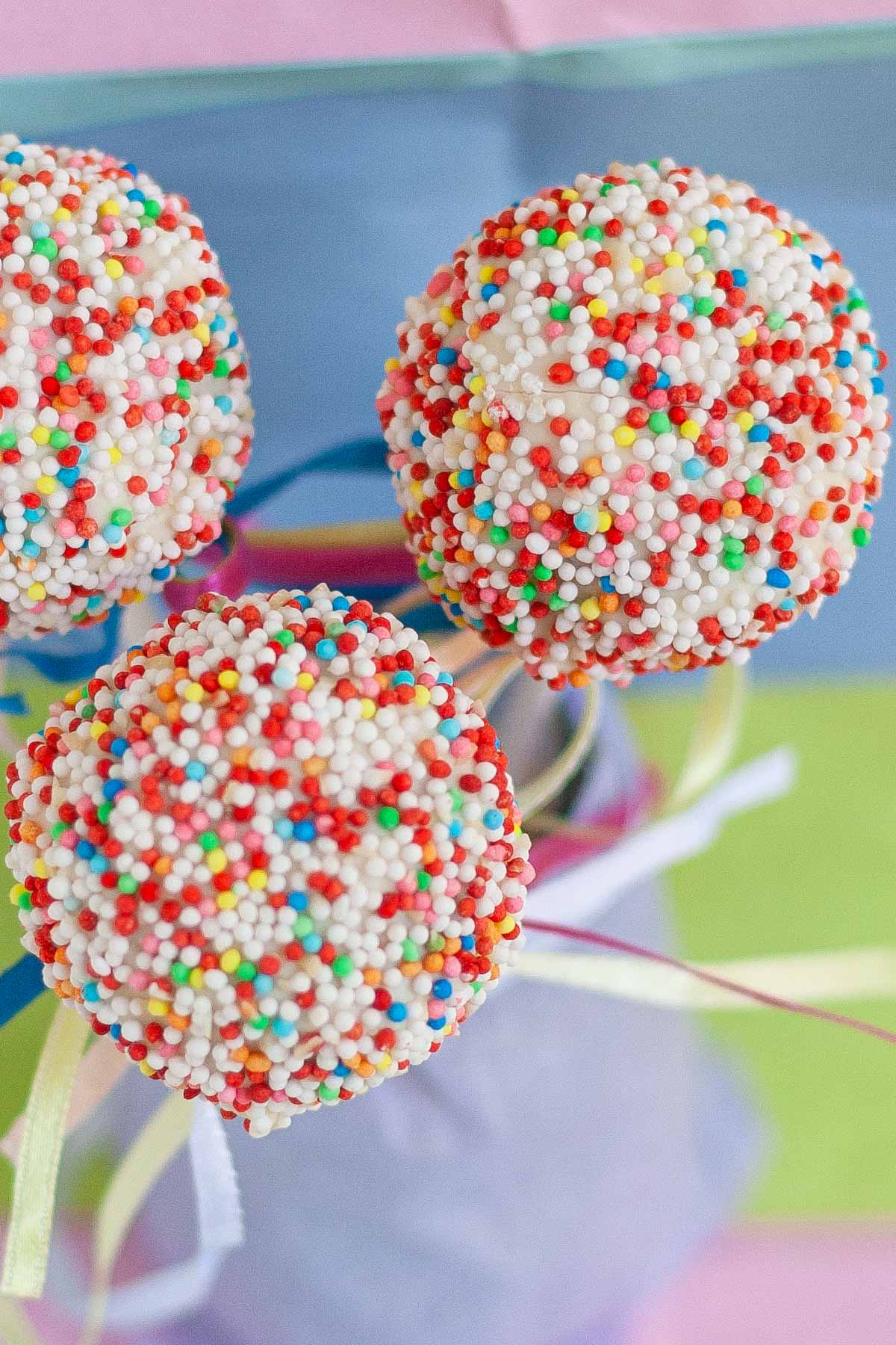 Three cake pops decorated with colorful candy sprinkles.