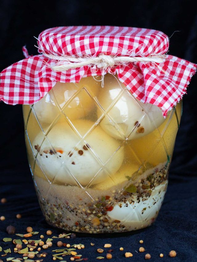 Glass jar of pickled egg with red checkered cloth lid cover.