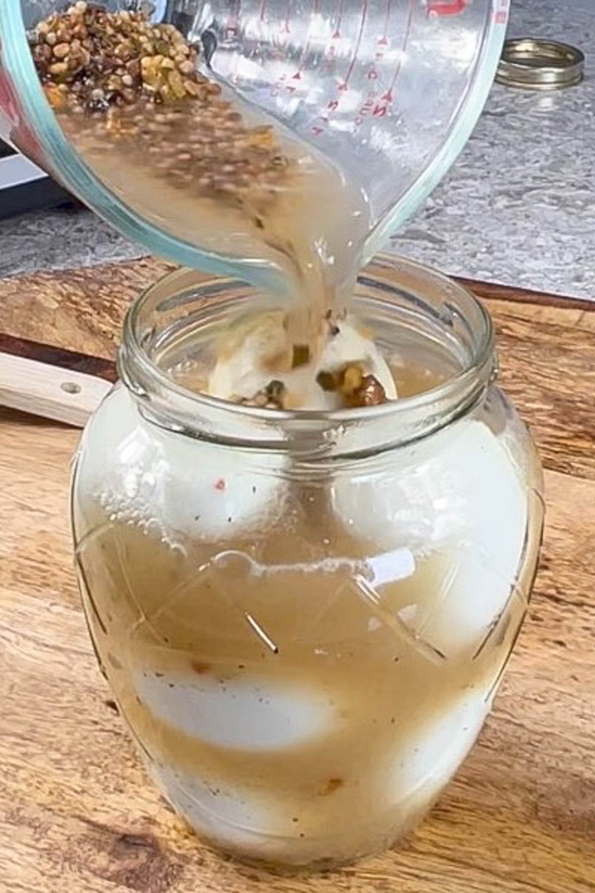 Pickle brine being poured over hard boiled eggs in glass jar.
