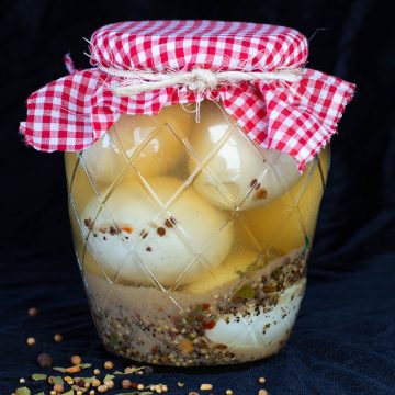 Glass jar of pickled egg with red checkered cloth lid cover.