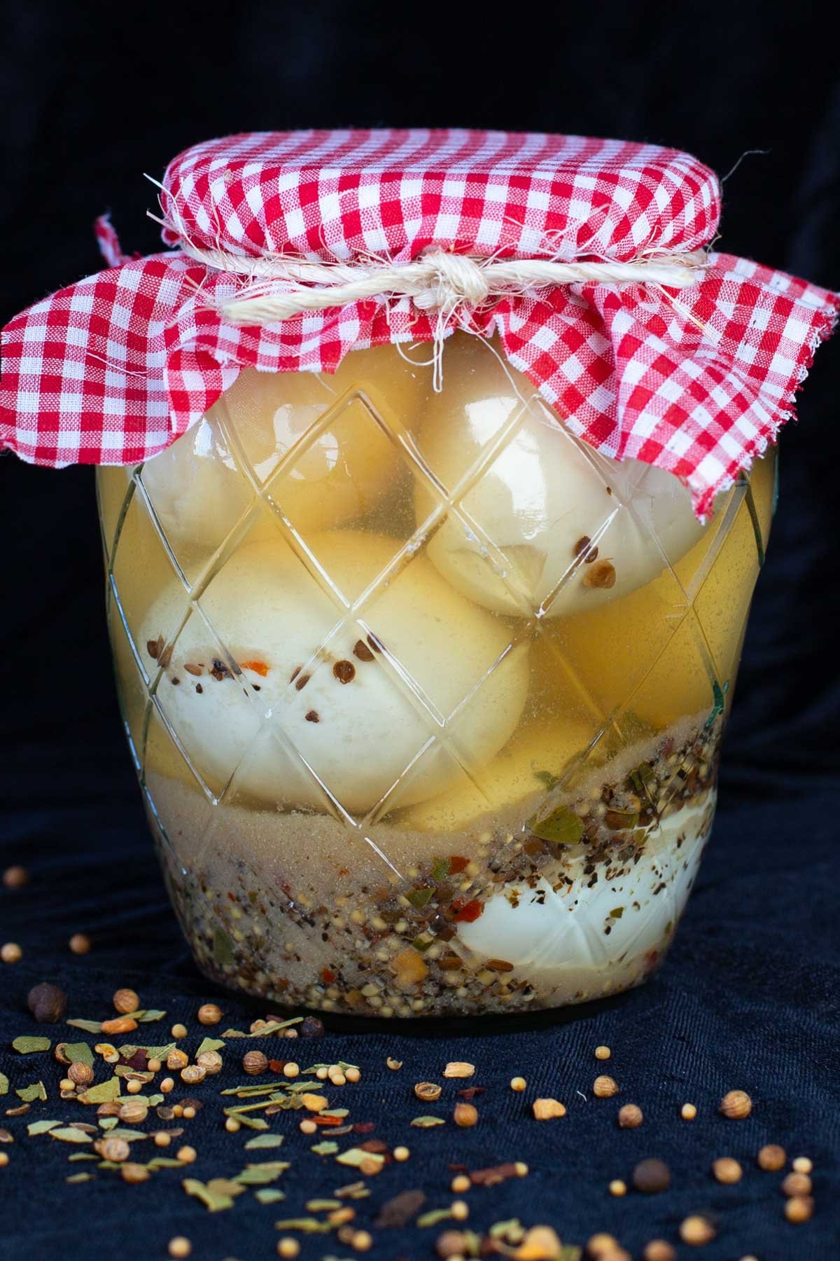 Glass jar of pickled egg with red checkered cloth lid cover.