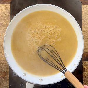 Brown sauce simmering in white skillet with black whisk.