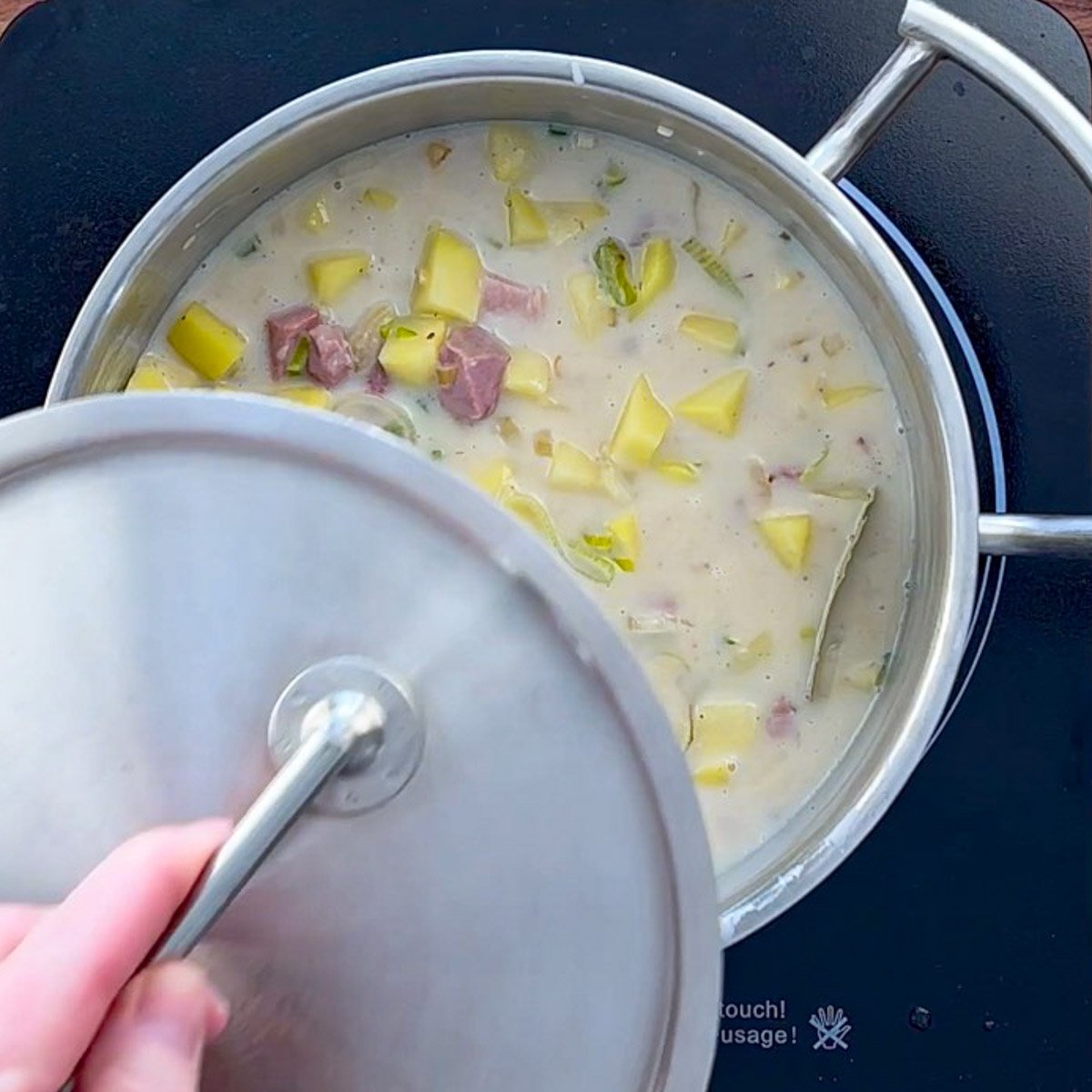 Lid being put onto large saucepan of ham and potato soup.