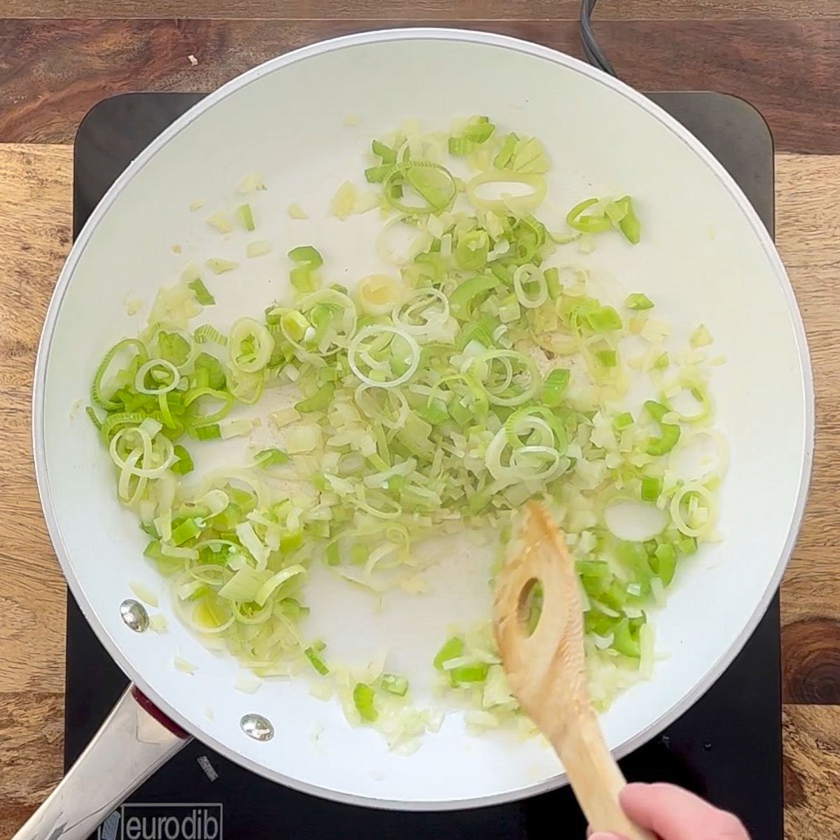 Onions, leeks, celery and garlic sautéing in white skillet.