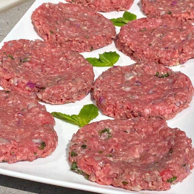 Plate of uncooked beef patties, garnished with mint leaves.