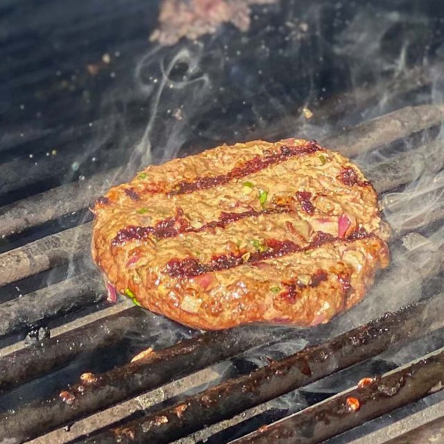 Beef patty grilling on barbecue.