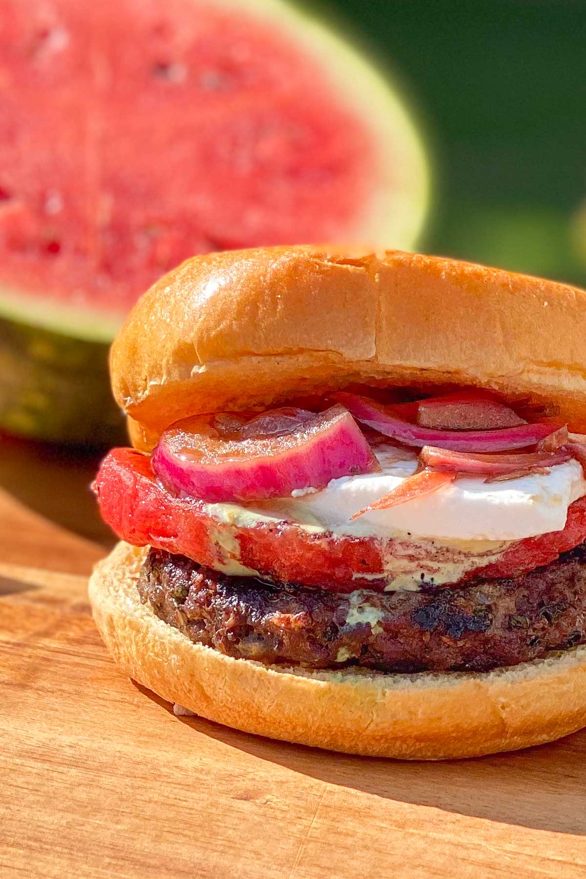Grilled beef burger with watermelon, feta cheese, and red onions, whole watermelon in background.