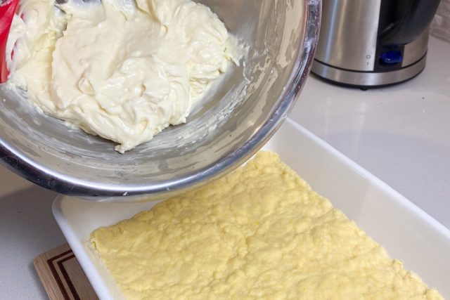 Bowl of cream cheese mixture being poured onto lemon cake crust.