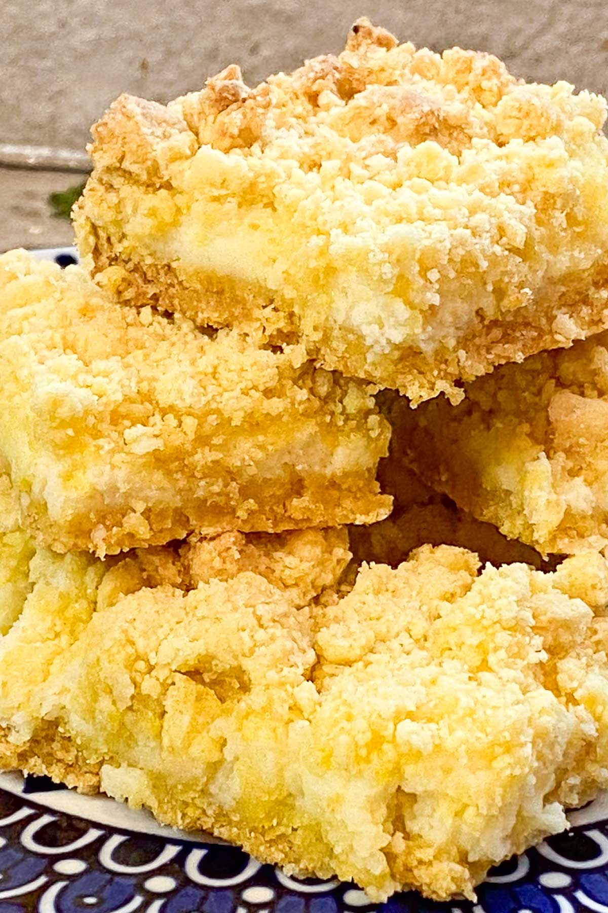 Stack of lemon bars with crumbly topping on decorative blue plate.