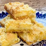 Stack of lemon bars with crumbly topping on decorative blue plate.