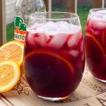 Glasses of red wine with orange slice and ice cubes.