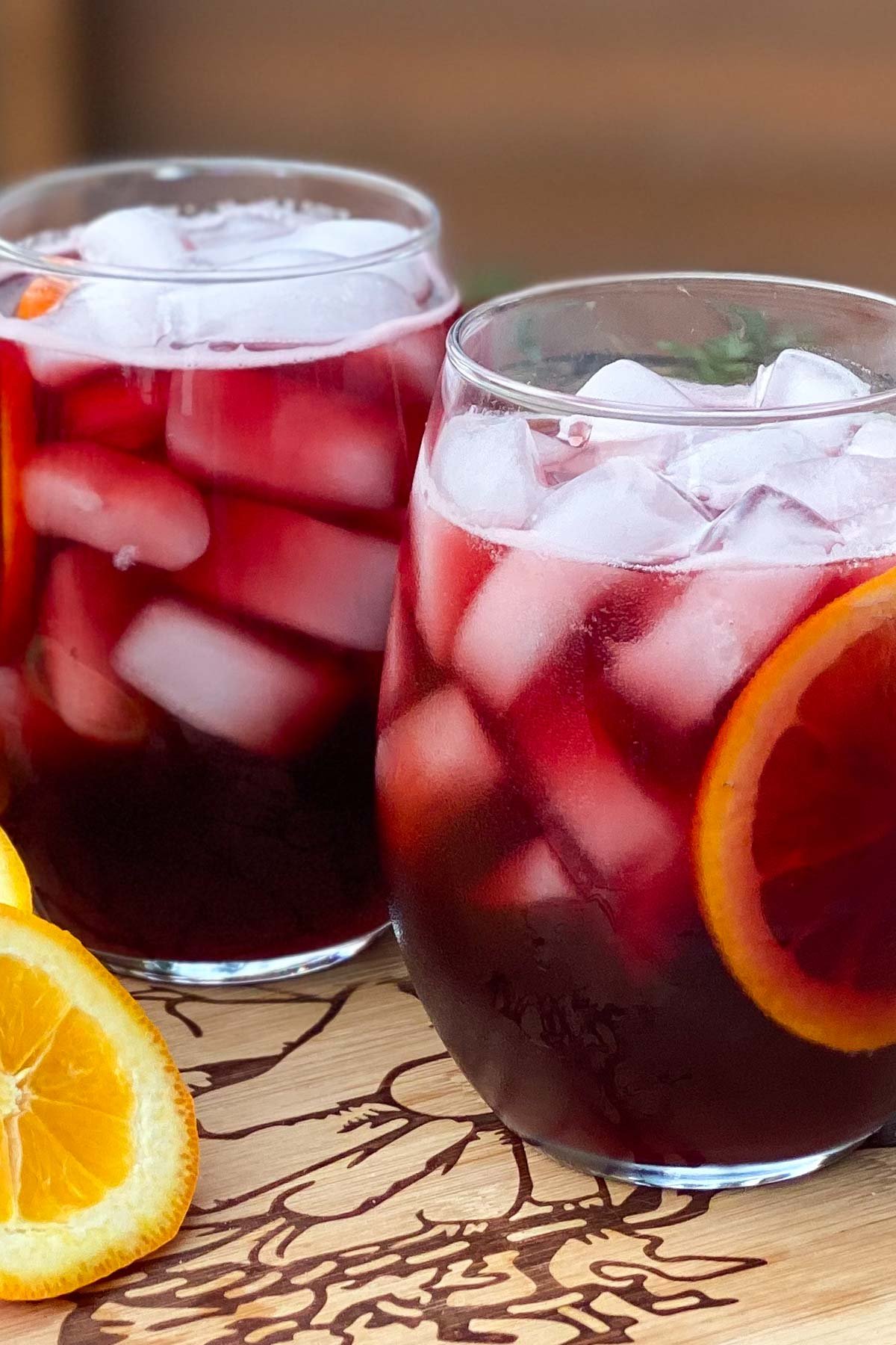 Glasses of red wine with orange slice and ice cubes.