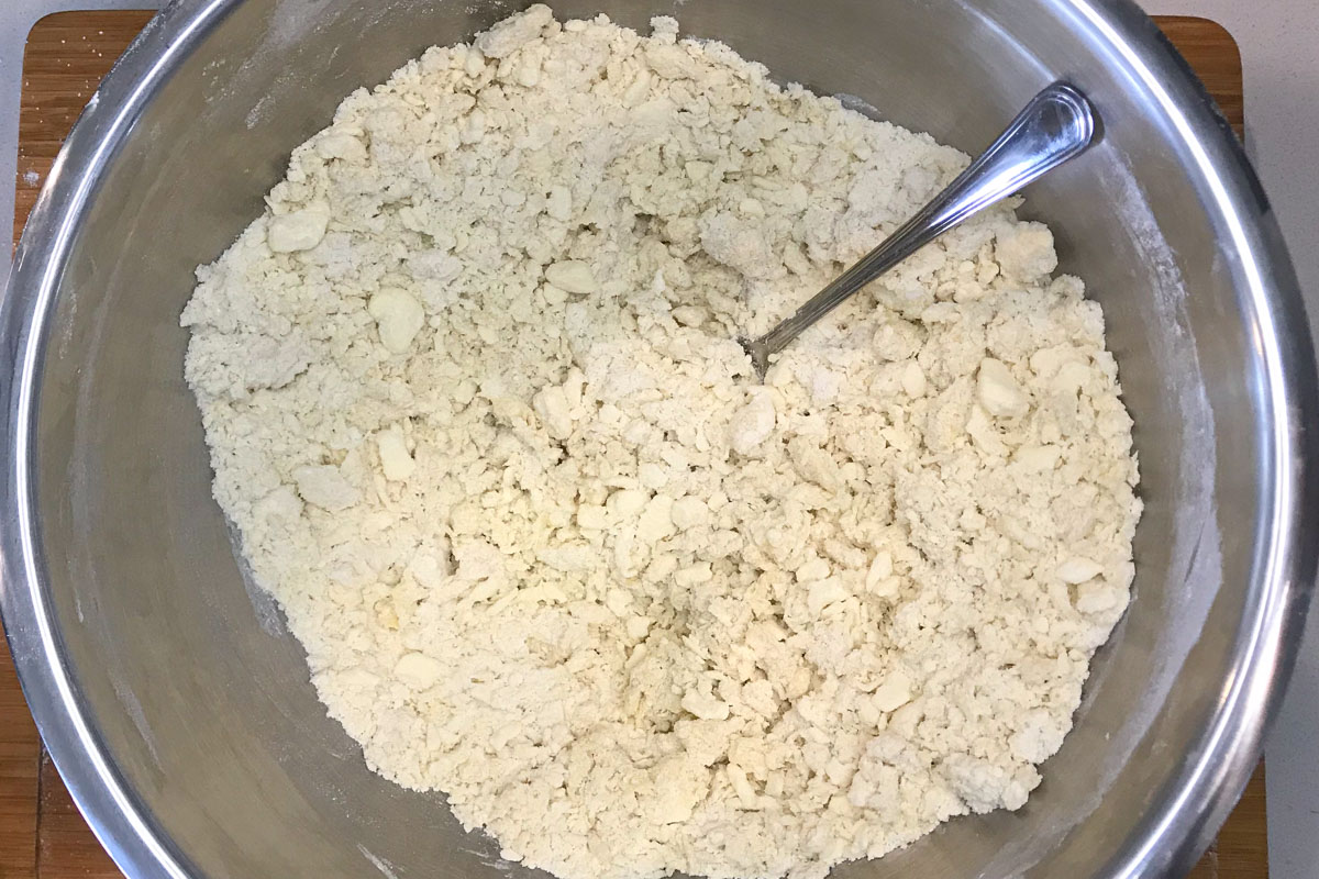 Crumble mix of flour and butter in a stainless steel bowl.