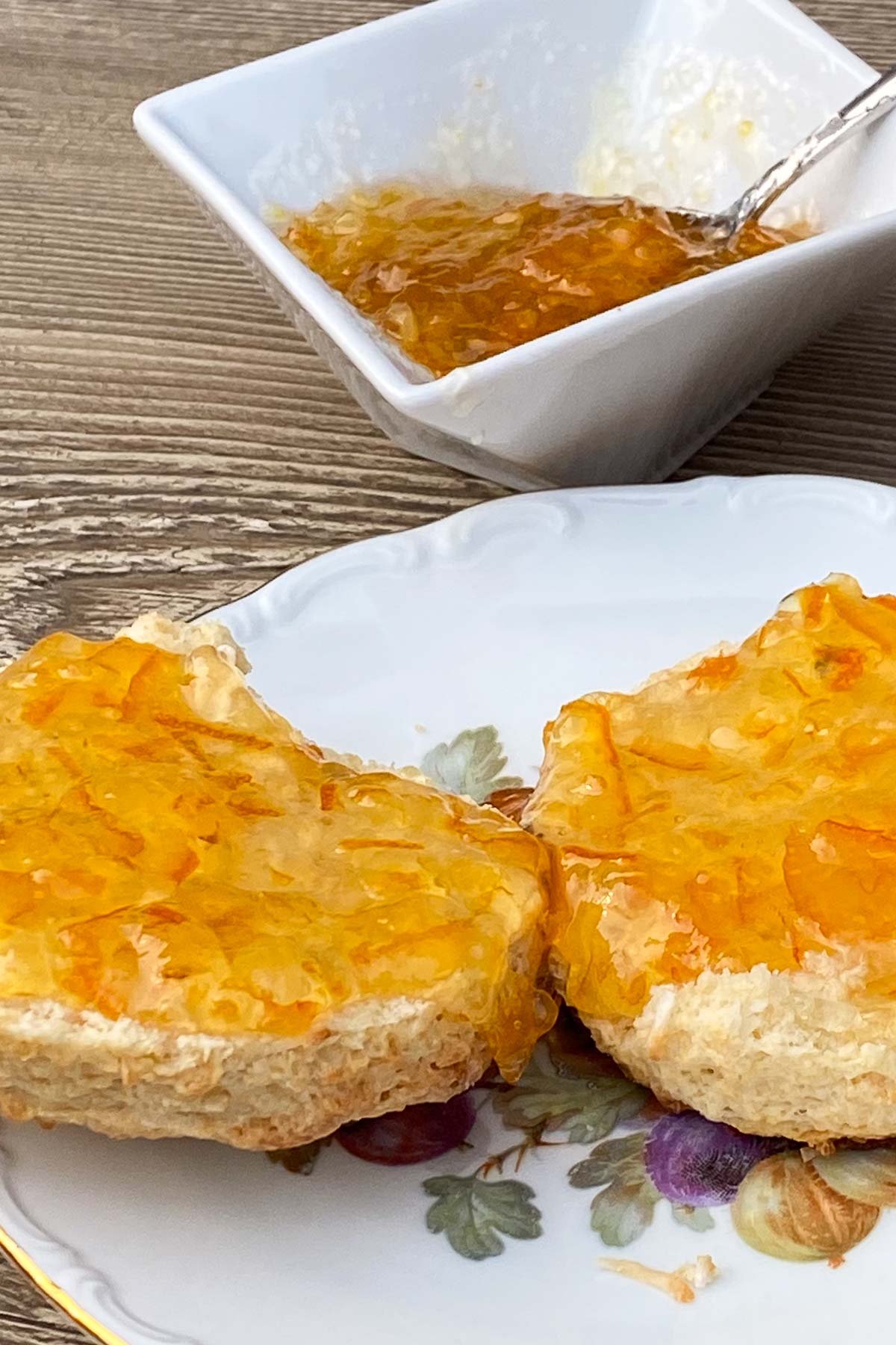 Scones topped with peach jam on decorative plate.