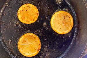 Three lemon slices frying in a cast iron skillet.