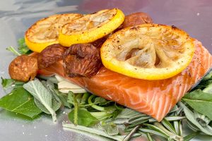 Uncooked salmon fillet on bed of fresh herbs and garlic, topped with figs and seared lemon slices.