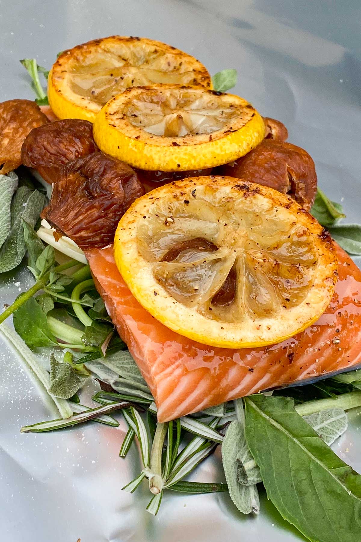 Uncooked salmon fillet on bed of fresh herbs and garlic, topped with figs and seared lemon slices.