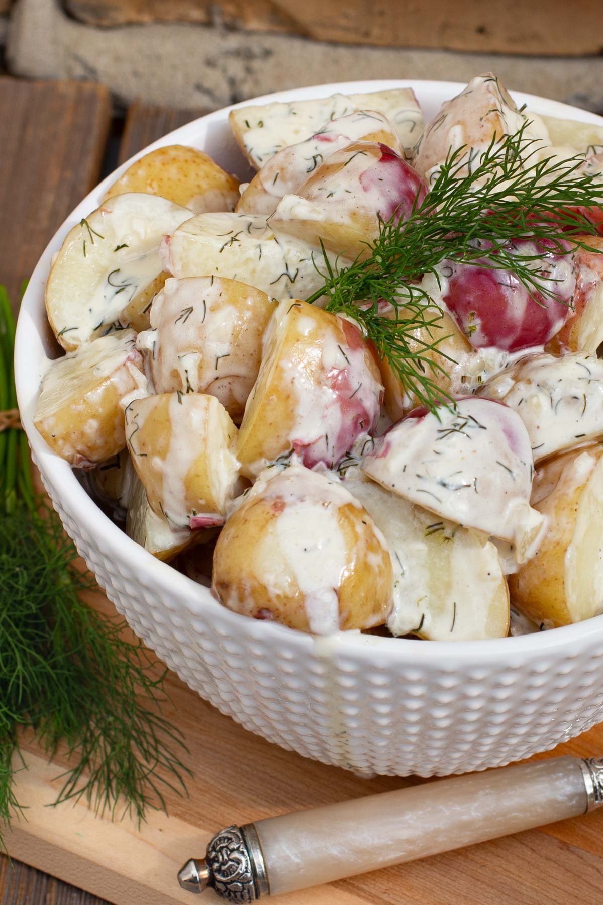 Potatoes covered in a creamy dill sauce in a white bowl.