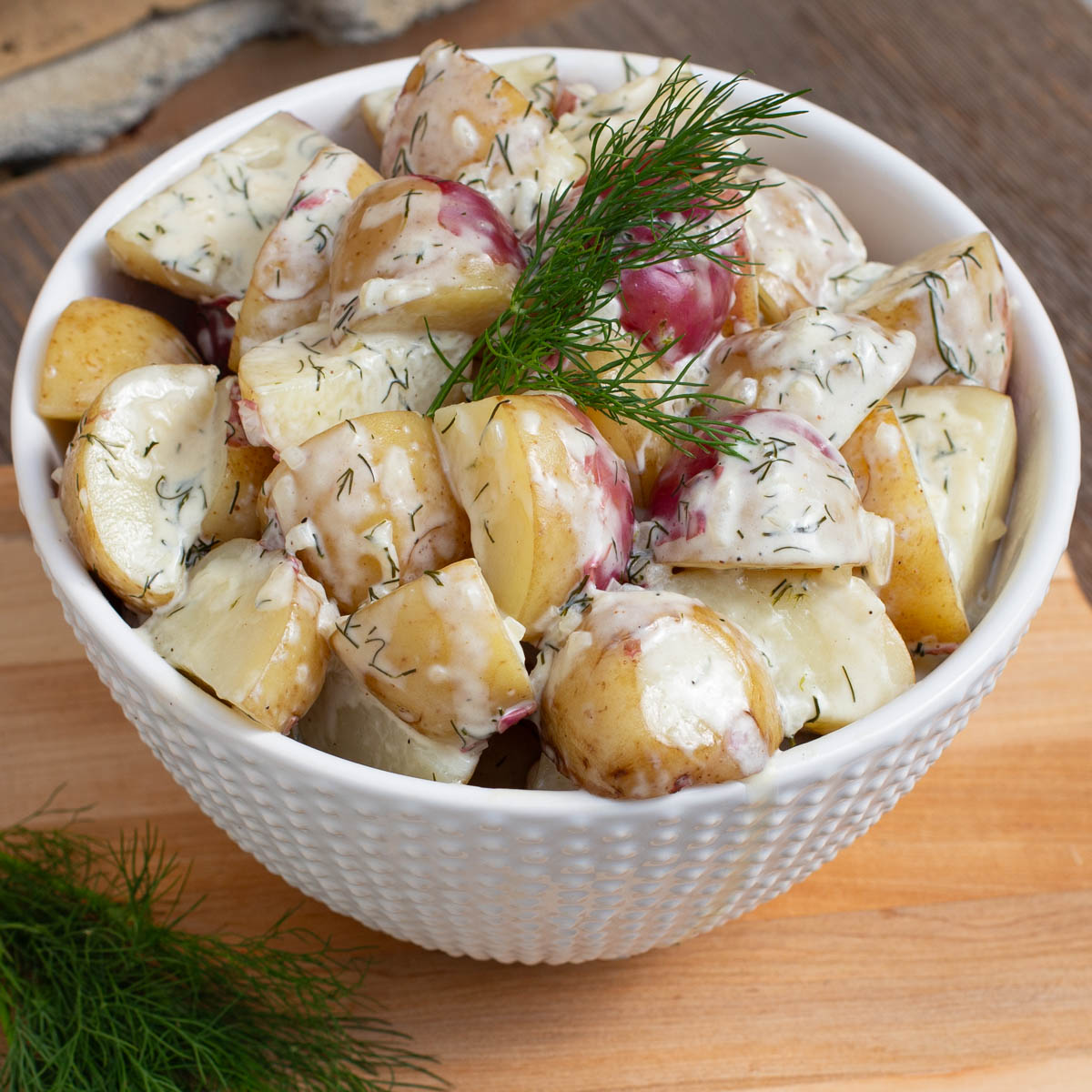 Potatoes covered in a creamy dill sauce in a white bowl.