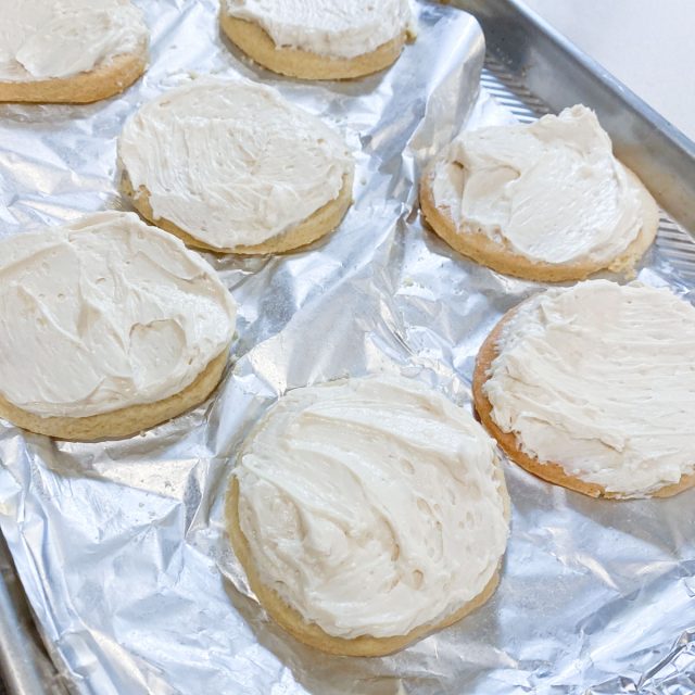 Cookies topped with cream cheese on foil lined baking sheet.