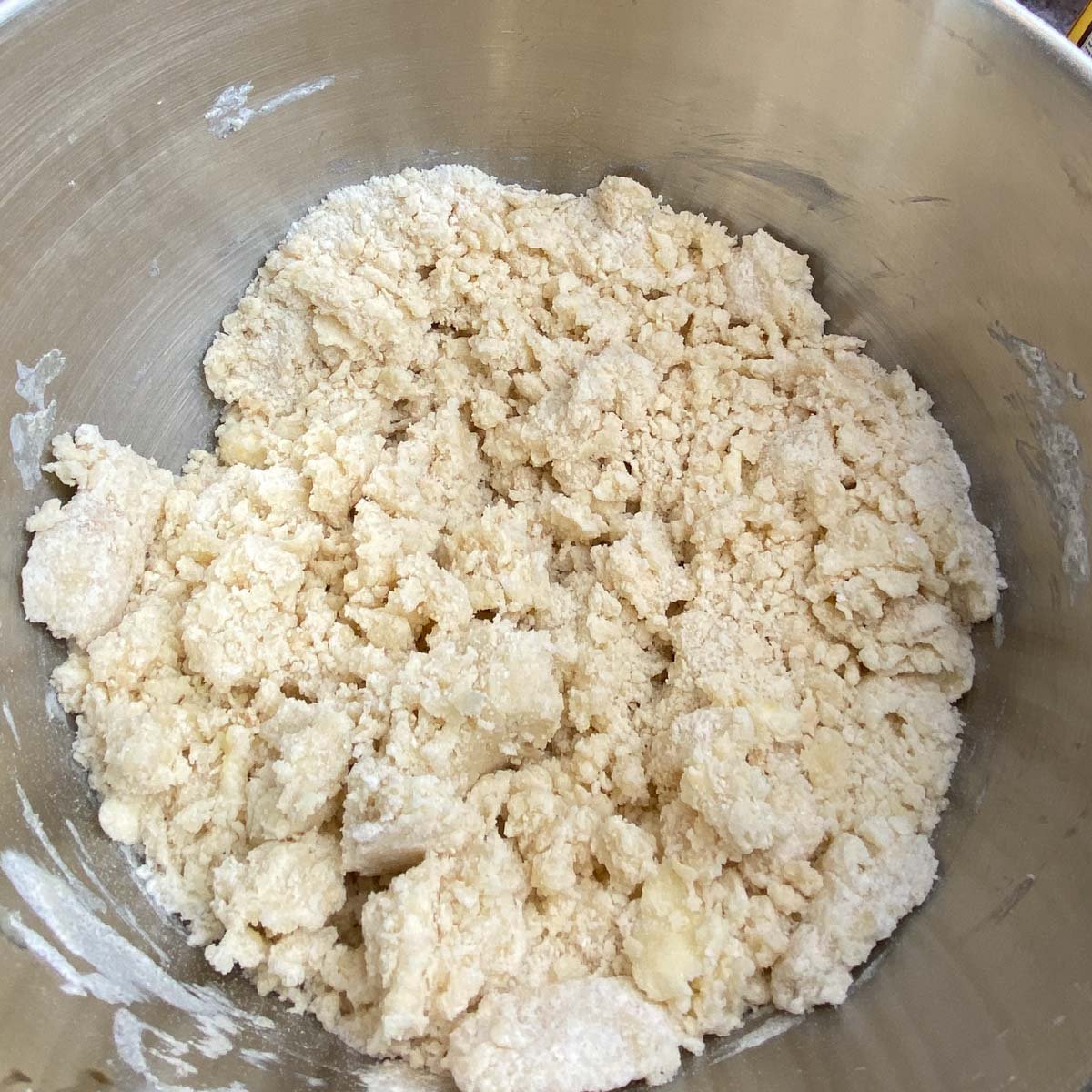 Chunks of blended sugar cookie dough in a large stainless steel mixing bowl.