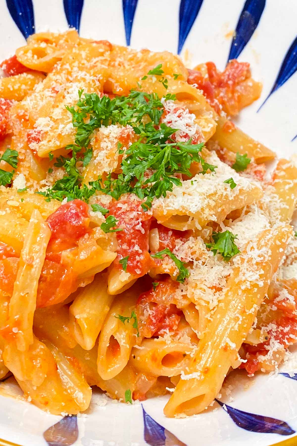 Penne pasta and tomato sauce, garnished with parsley in blue and white decorative bowl.