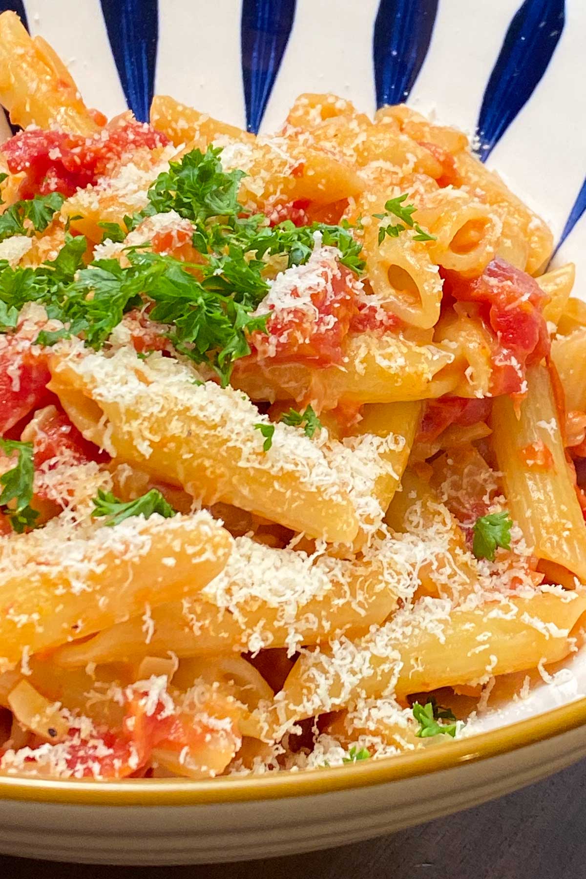 Penne pasta and tomato sauce, garnished with parsley in blue and white decorative bowl.