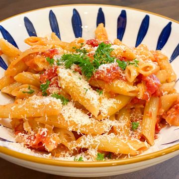Penne pasta and tomato sauce, garnished with parsley in blue and white decorative bowl.
