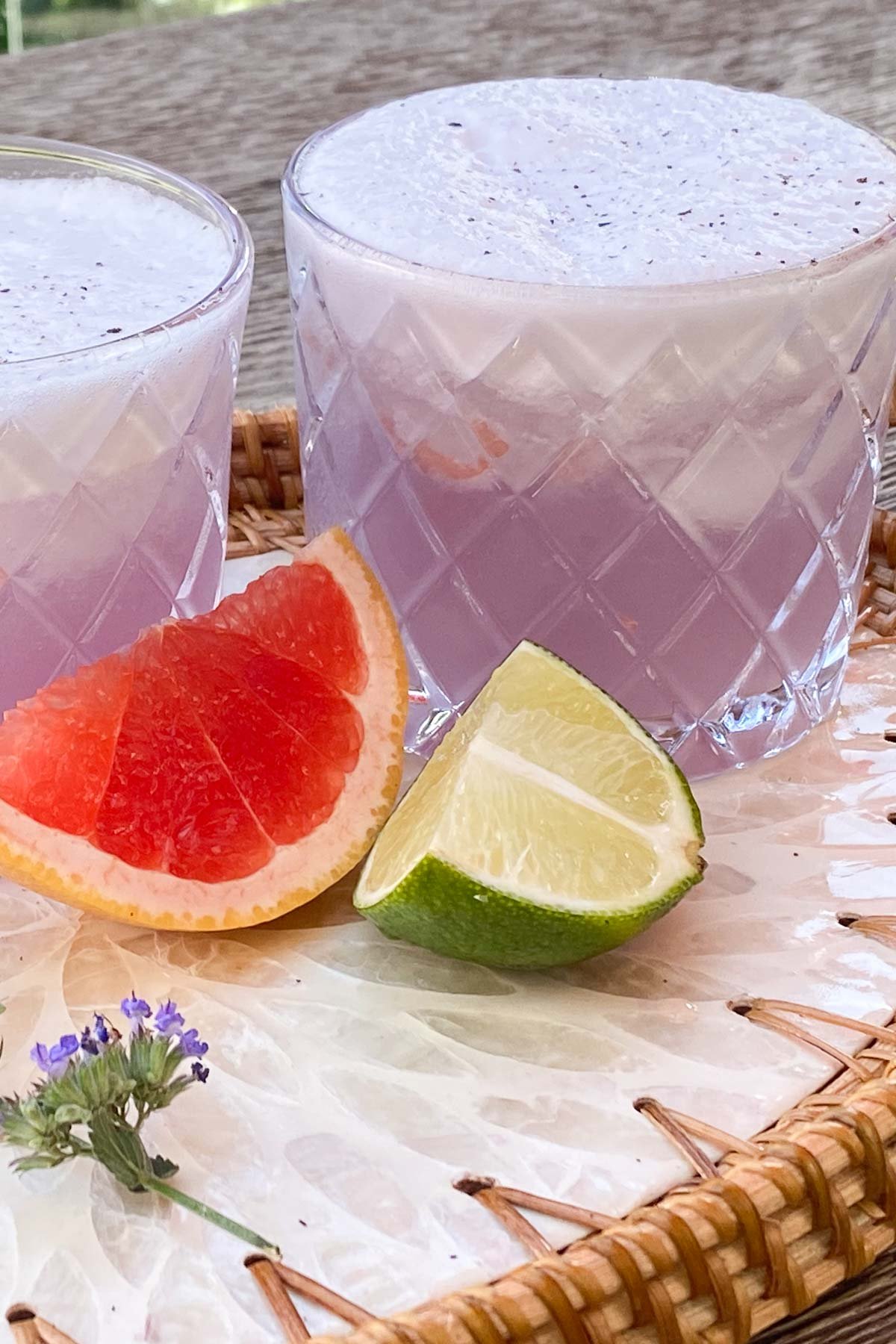 Short bar glass of pink cocktail with foam topping, background of wedges of grapefruit and lime.