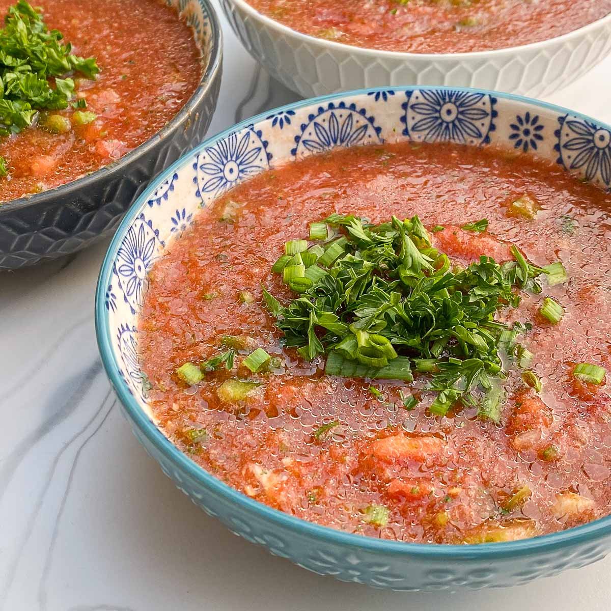 Blue bowls of gazpacho soup garnished with parsley and chives.