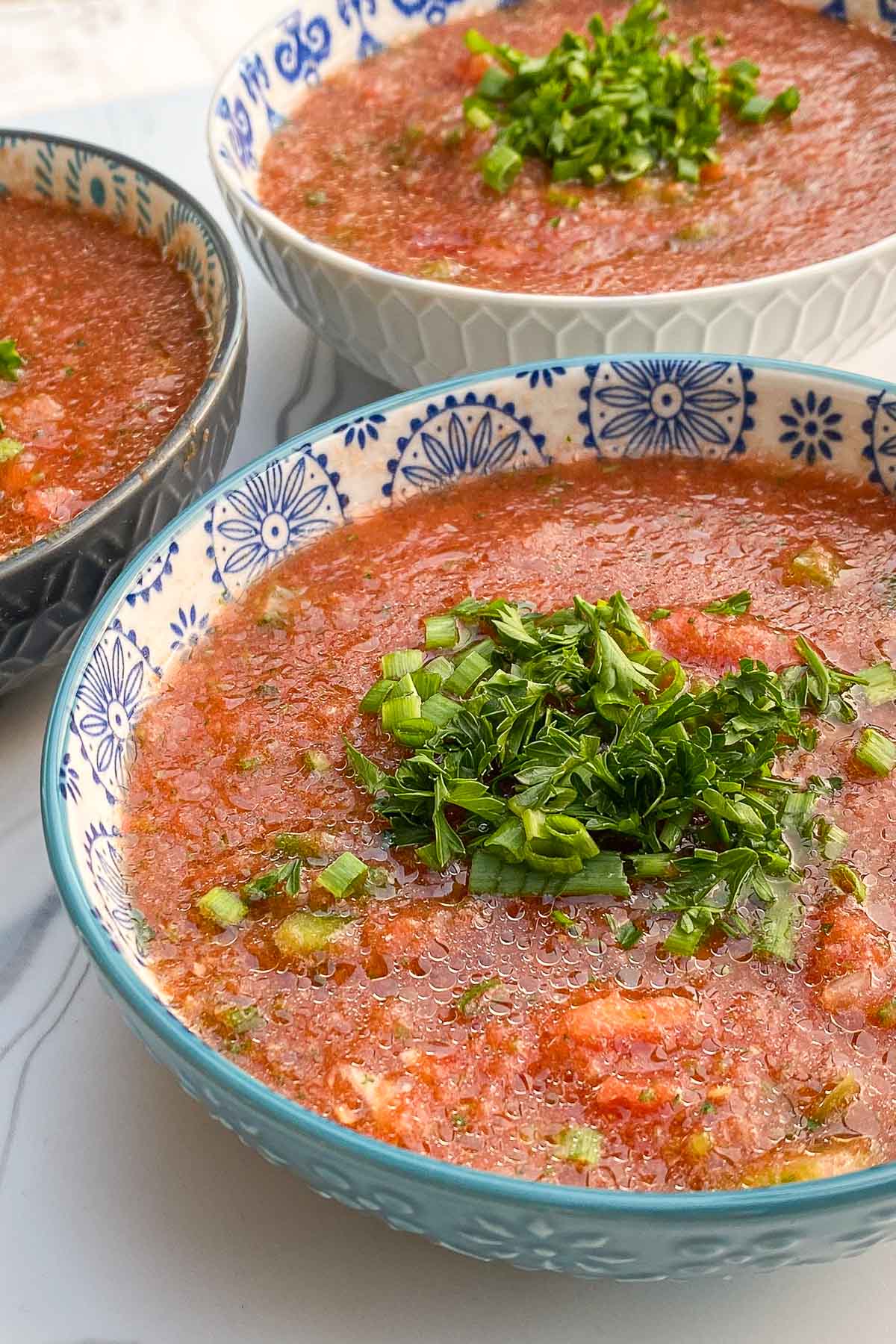 Blue bowls of gazpacho soup garnished with parsley and chives.