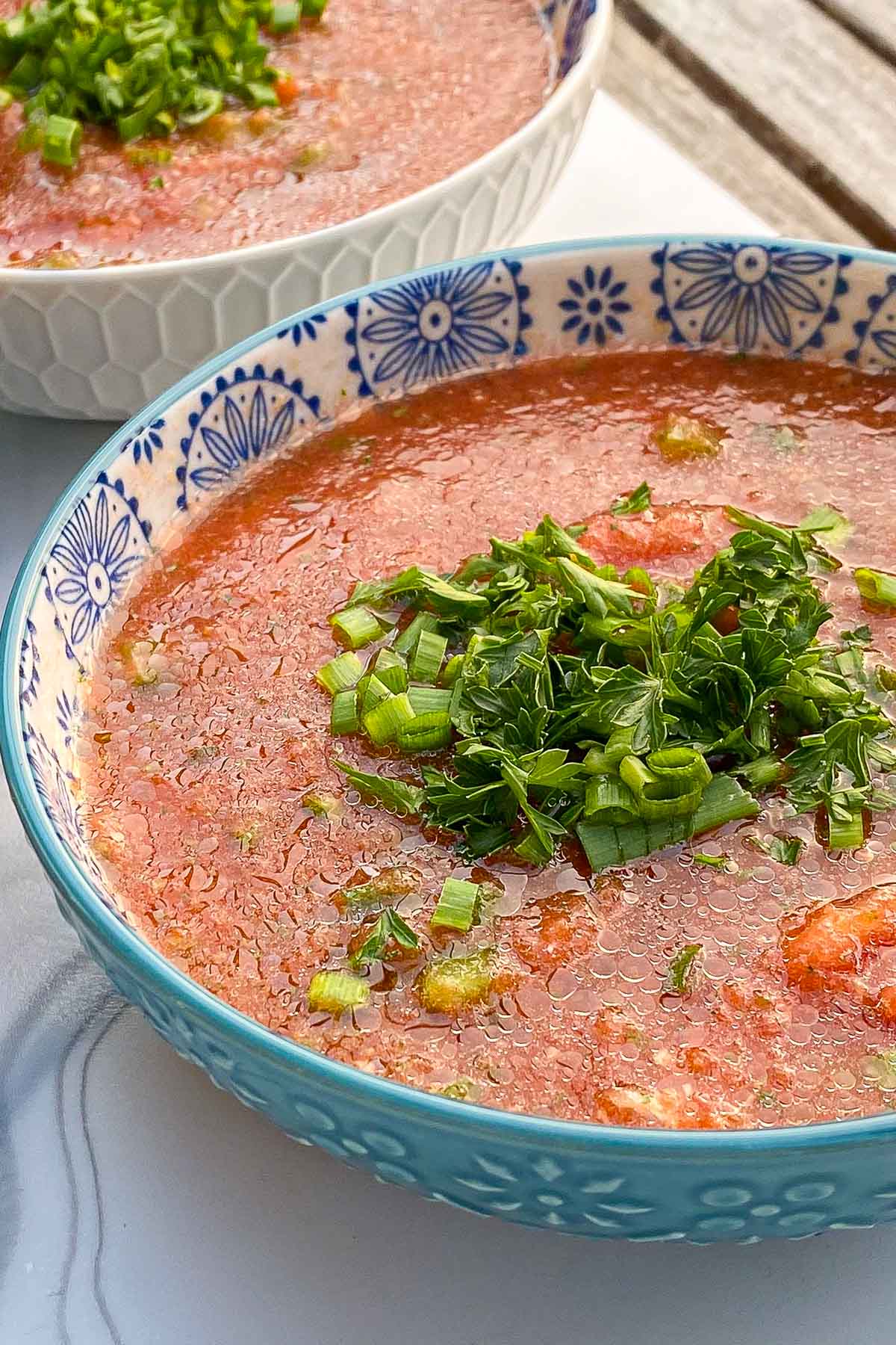 Blue bowls of gazpacho soup garnished with parsley and chives.