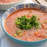 Blue bowls of gazpacho soup garnished with parsley and chives.