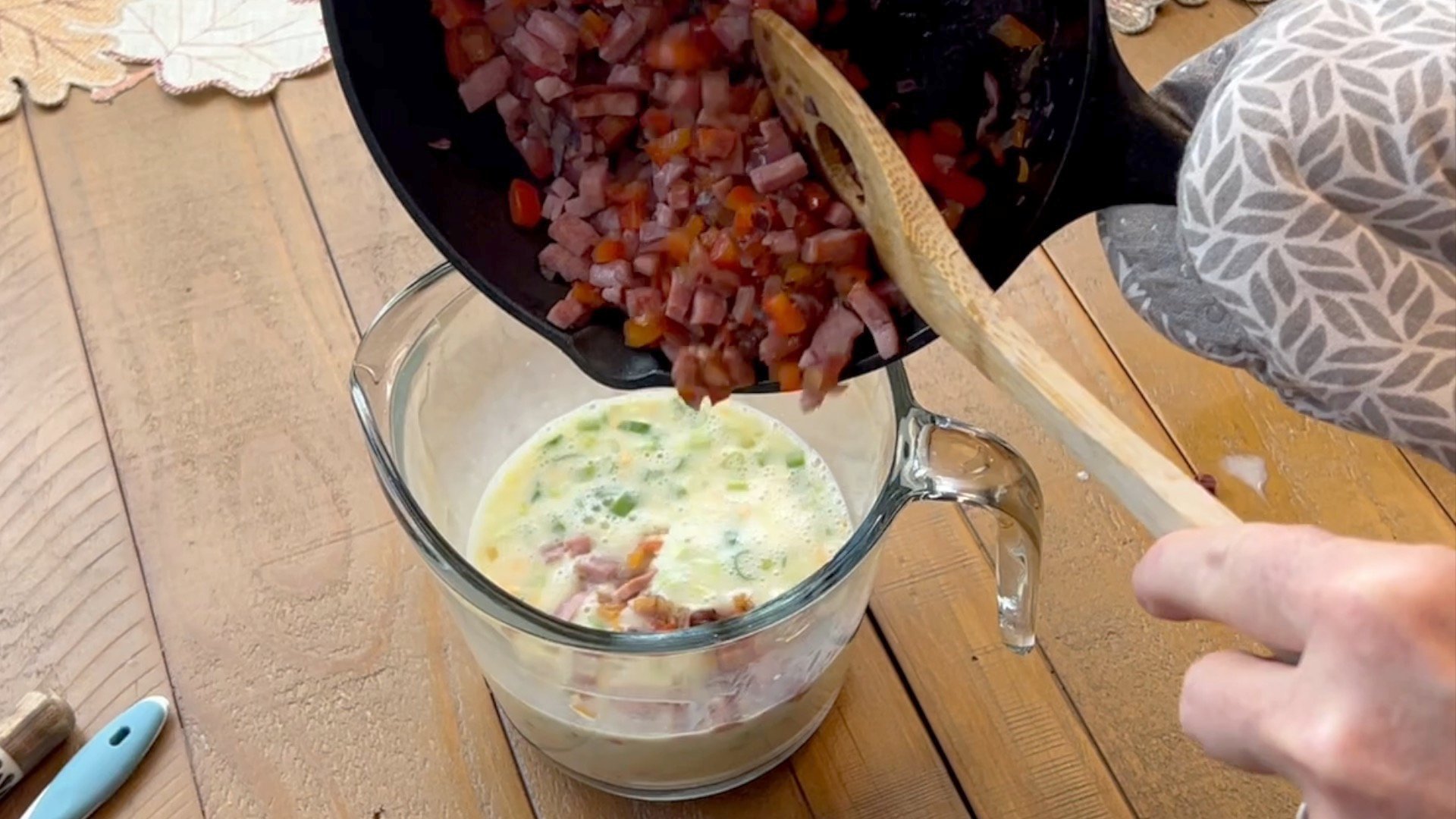 Pouring skillet of sautéed  ham and veggies into egg mixture in large measuring cup.