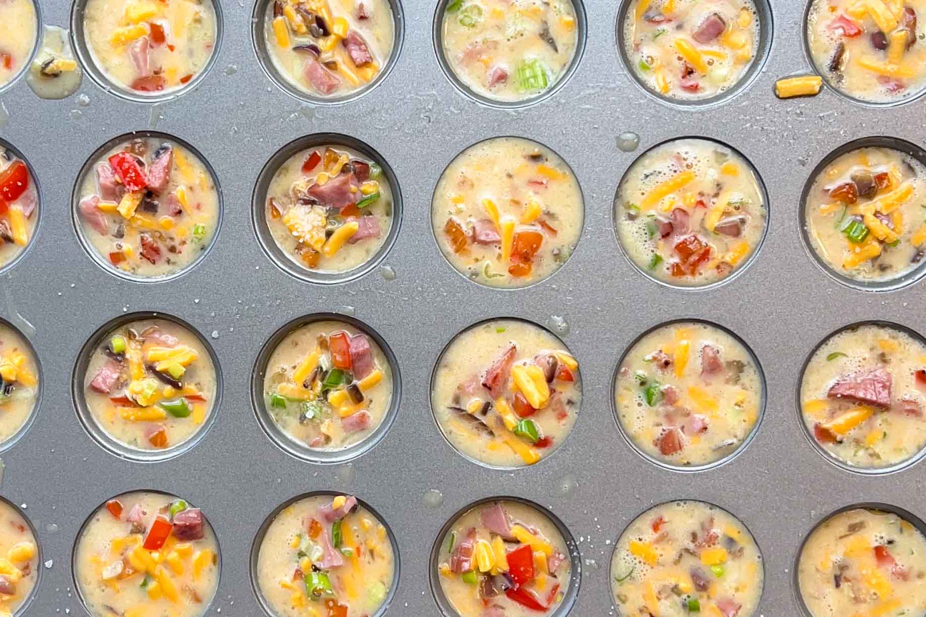 Mini muffin pan filled with egg, veggie and ham mixture.