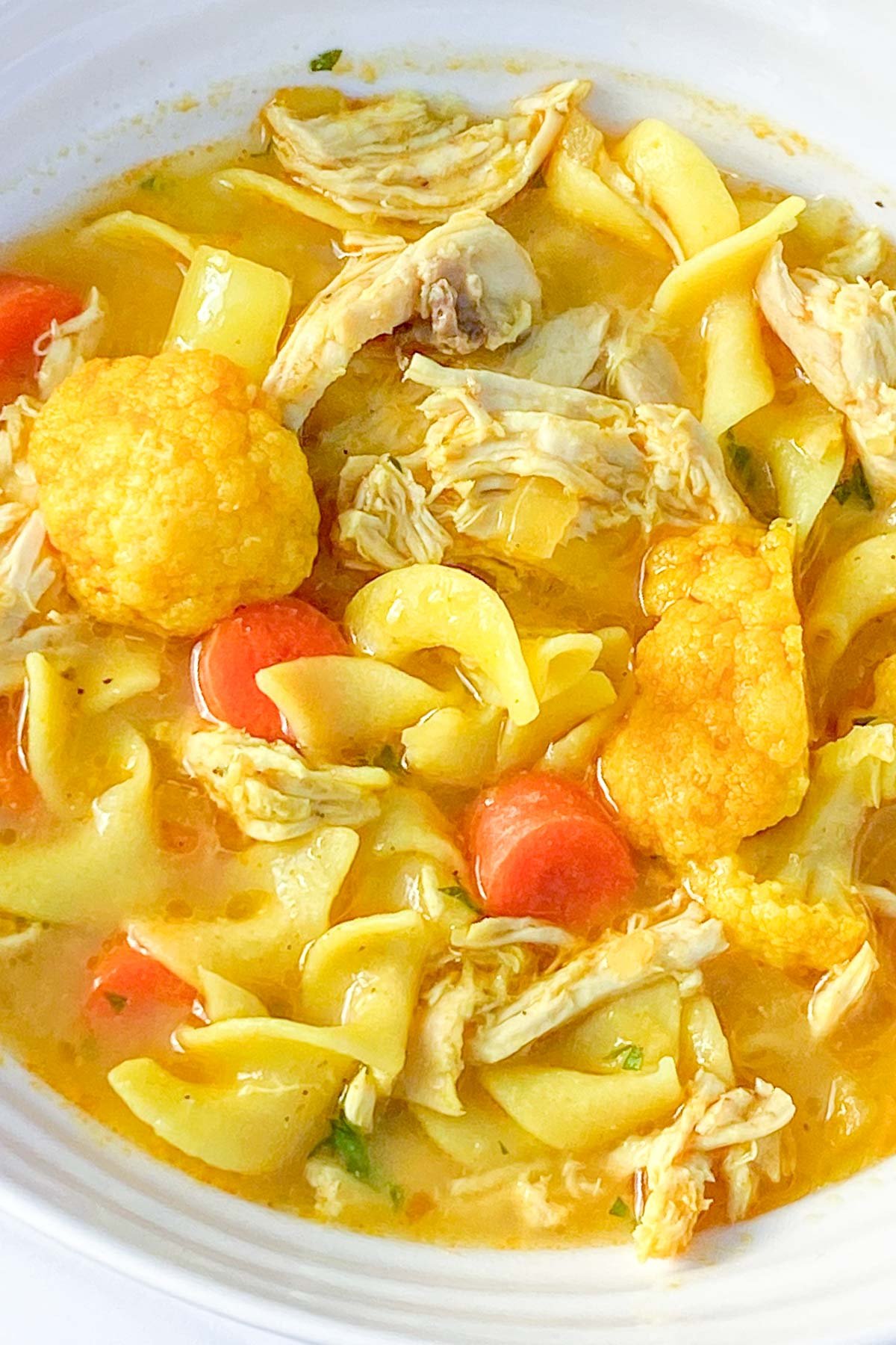 Bowl of soup with chicken, cauliflower, carrots and broad noodles.