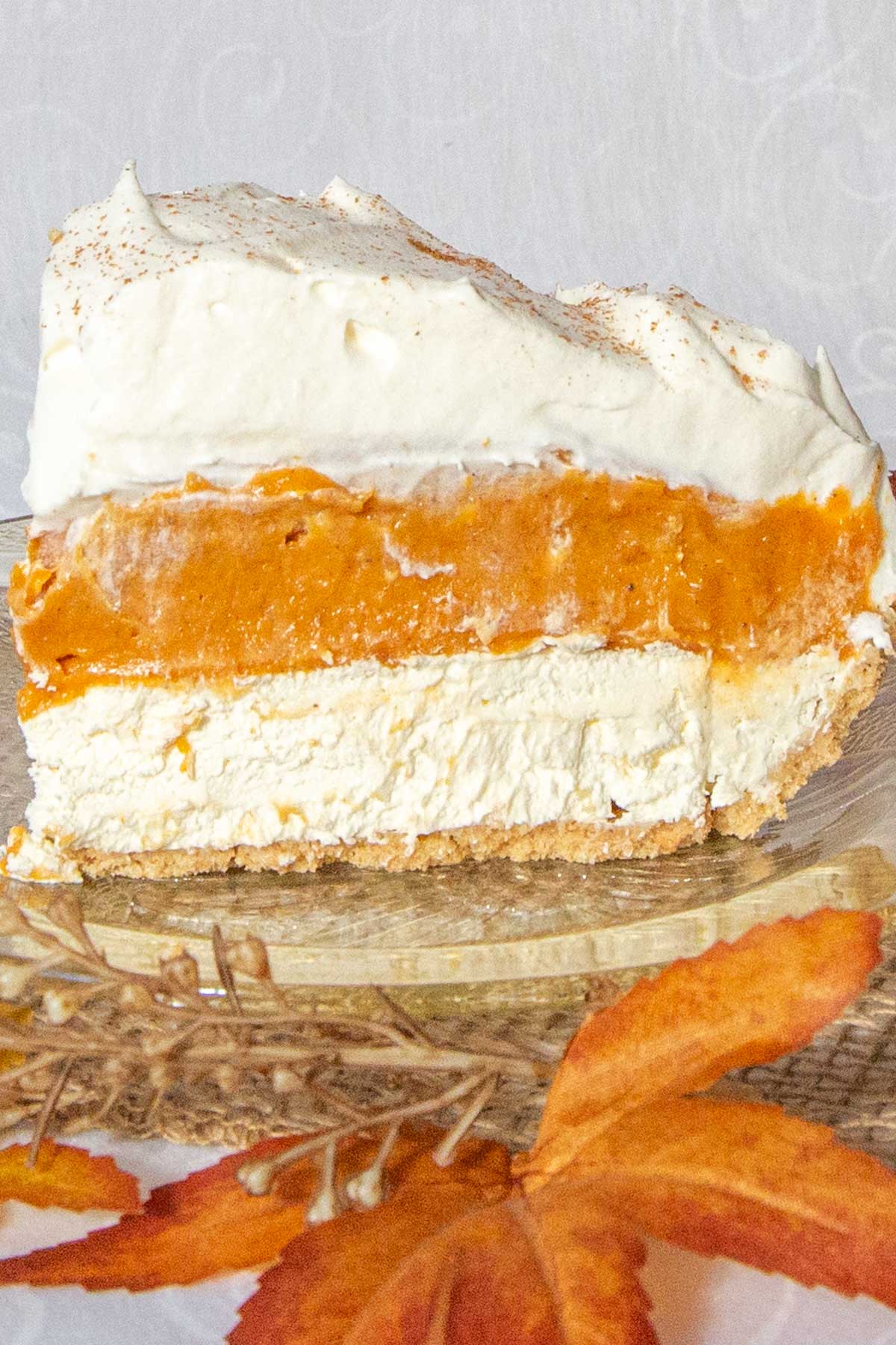 Slice of pumpkin pie with layers of pumpkin, cream cheese and whipped cream on amber coloured glass plate.