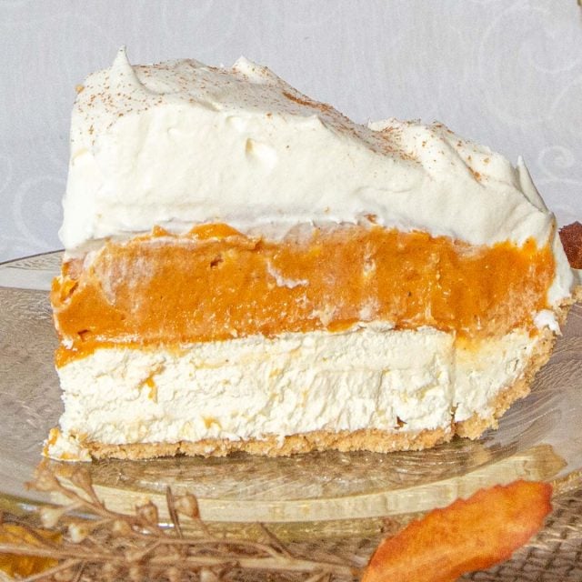 Slice of pumpkin pie with layers of pumpkin, cream cheese and whipped cream on amber coloured glass plate.