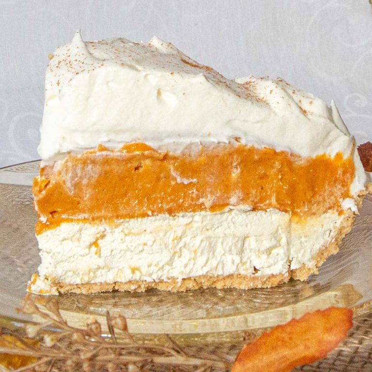 Slice of pumpkin pie with layers of pumpkin, cream cheese and whipped cream on amber coloured glass plate.