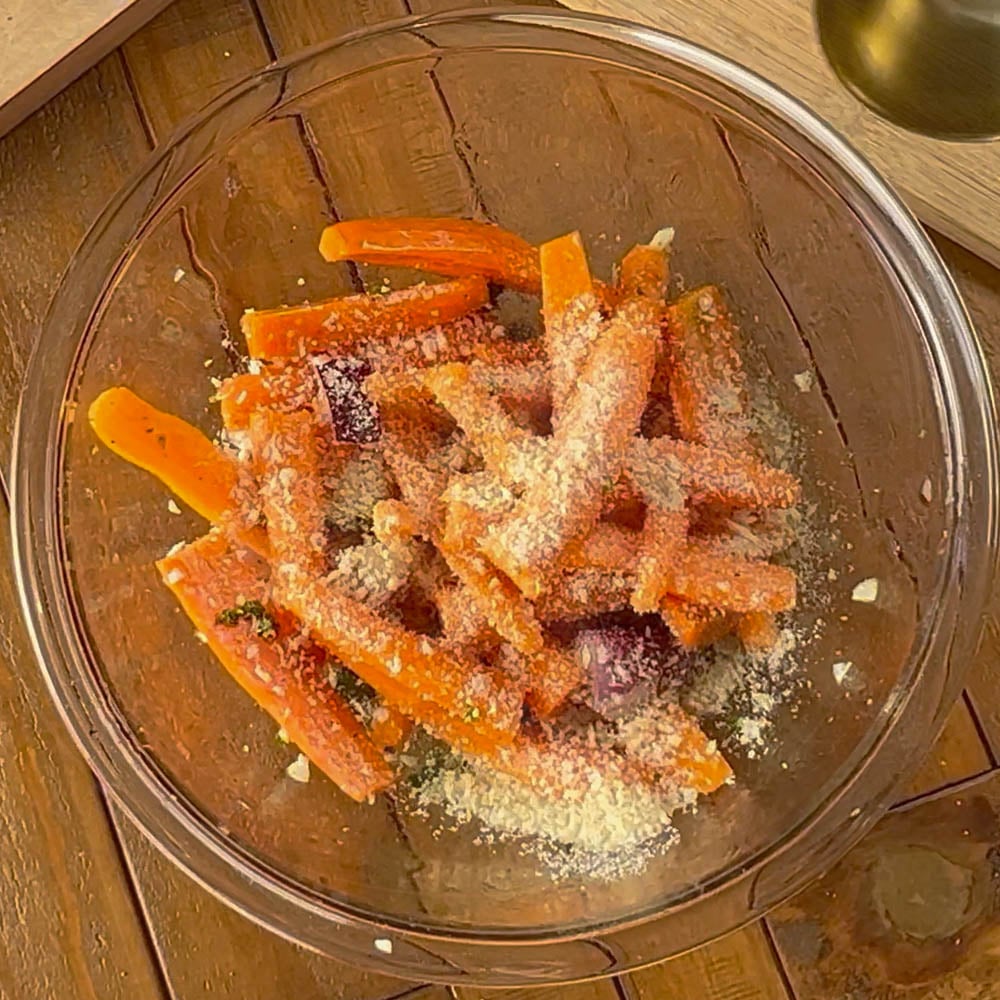 Glass bowl filled with raw sliced carrots, onions, sprinkled with breadcrumbs.