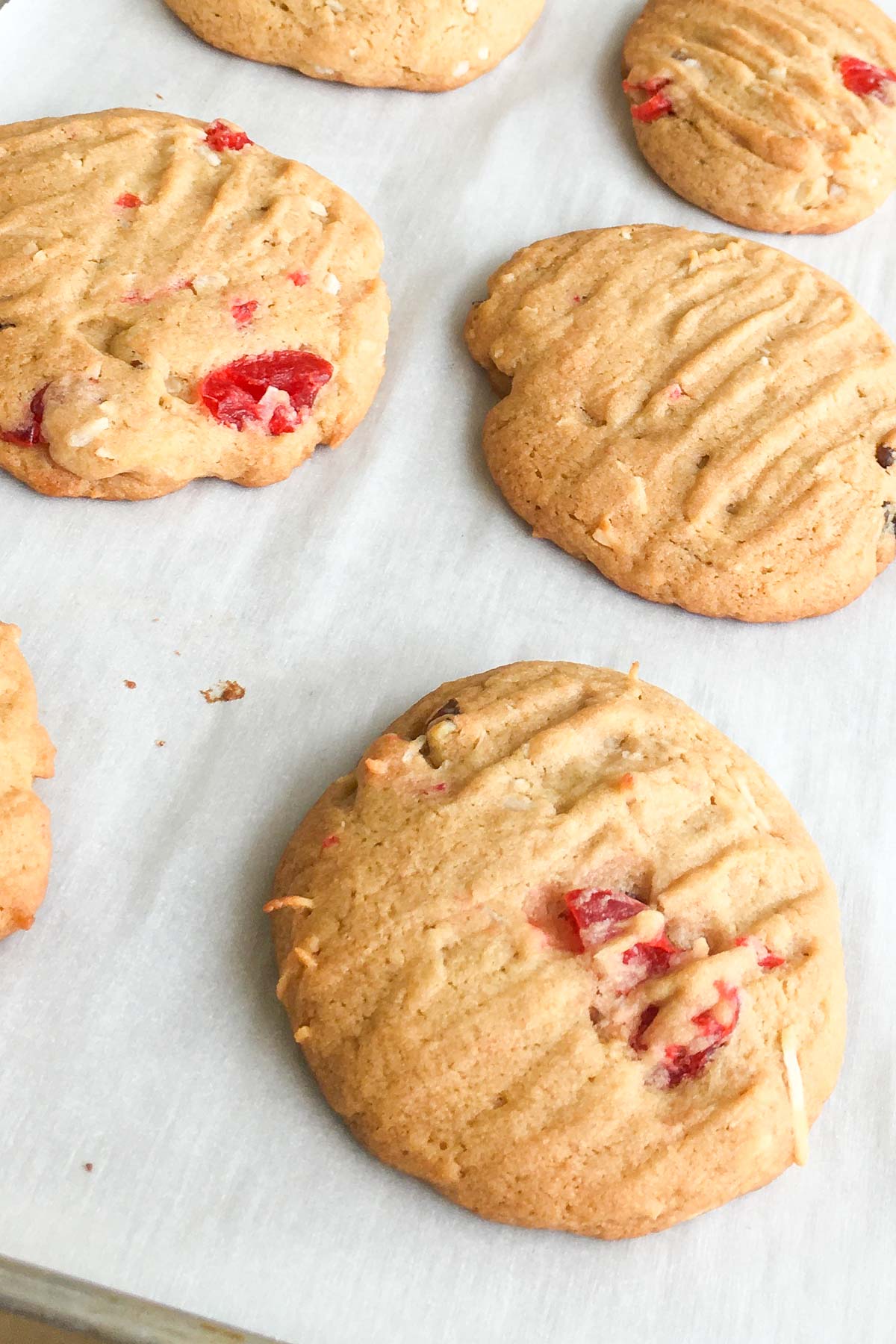 Baked cookies with maraschino cherries, walnuts and coconut on parchment lined baking pan.