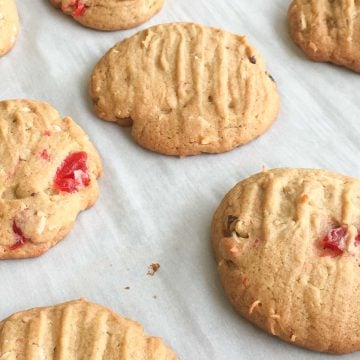 Baked cookies with maraschino cherries, walnuts and coconut on parchment lined baking pan.