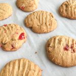 Baked cookies with maraschino cherries, walnuts and coconut on parchment lined baking pan.