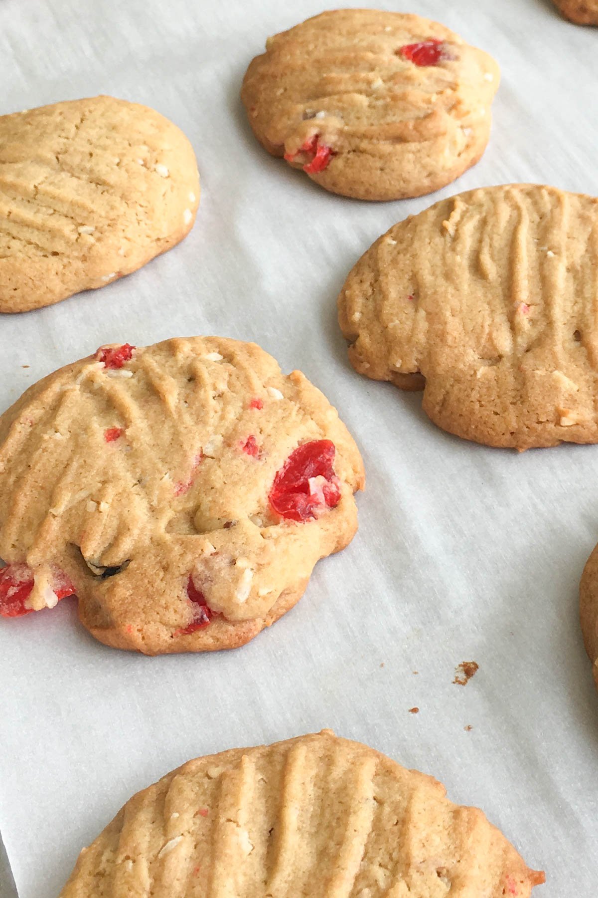 Baked cookies with maraschino cherries, walnuts and coconut on parchment lined baking pan.