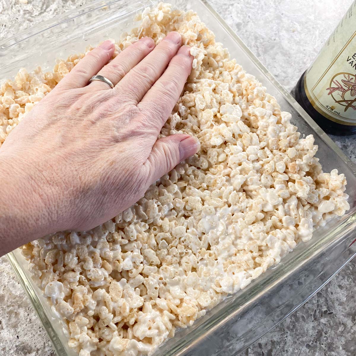Rice Krispie treat being pressed by hand into glass baking dish.