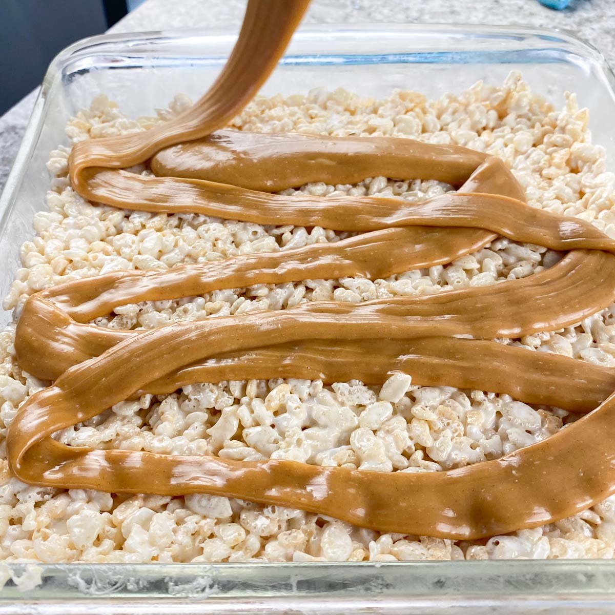 Caramel sauce being pour over Rice Krispie treat layer.