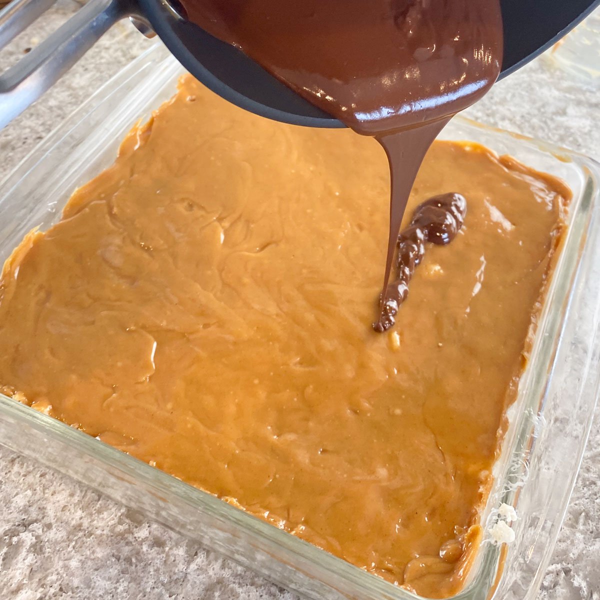 Melted chocolate pouring over caramel layer of Rice Krispie Squares.