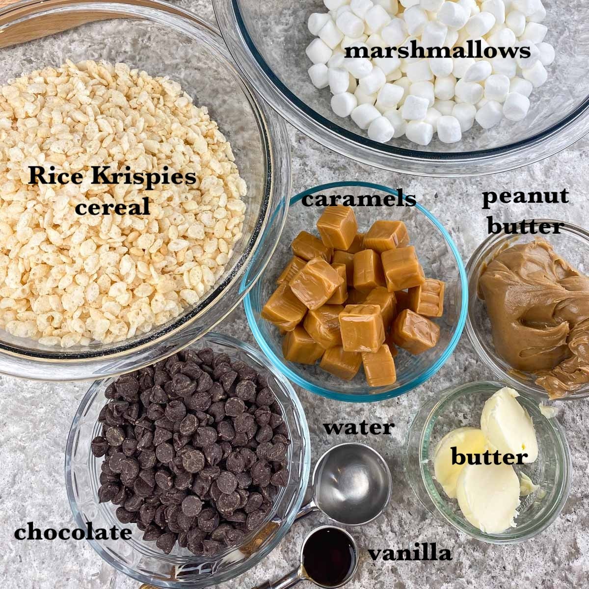 Ingredients measured in bowls, marshmallows, Rice Krispie cereal, caramels, peanut butter, chocolate, butter and vanilla extract.